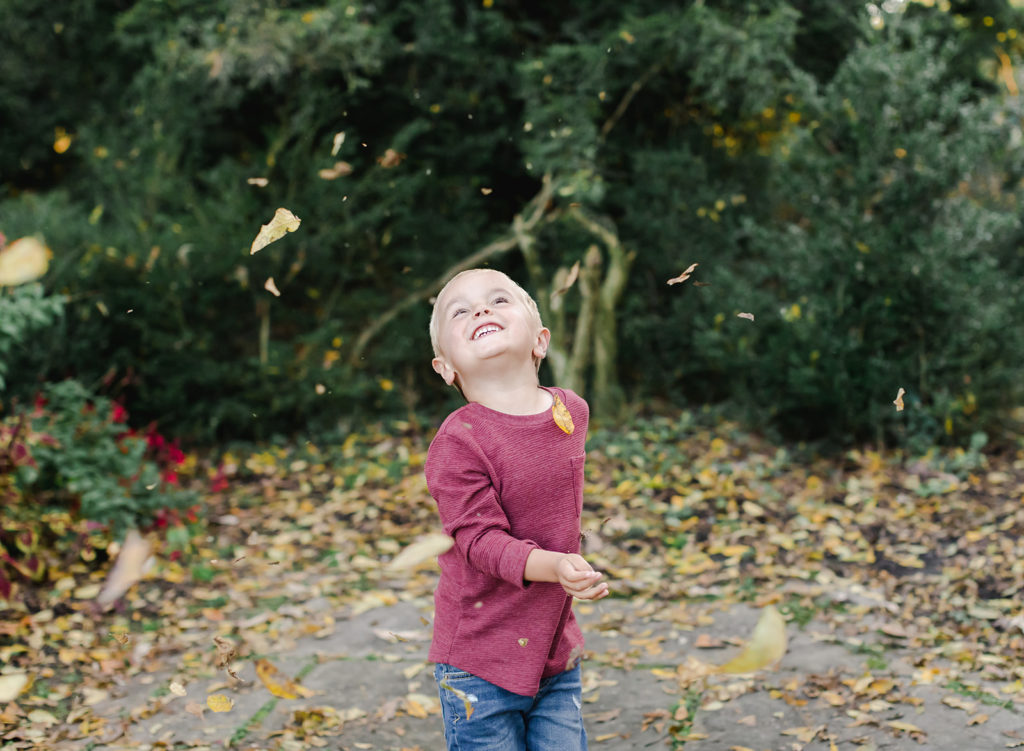 Young boy throwing leaves in the air and smiling